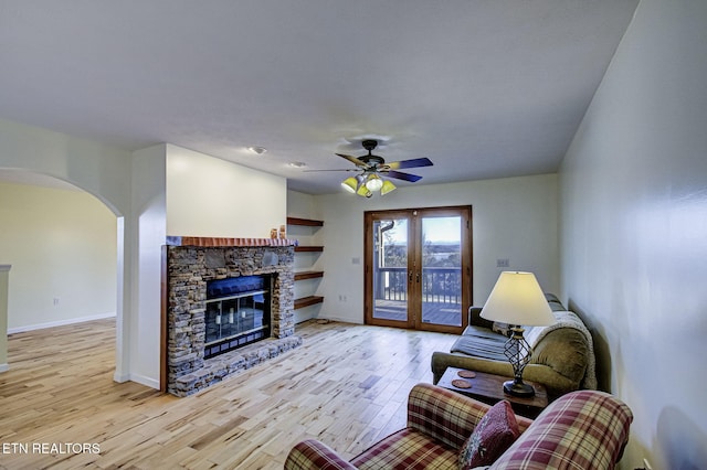 living room featuring french doors, ceiling fan, a fireplace, and light hardwood / wood-style floors