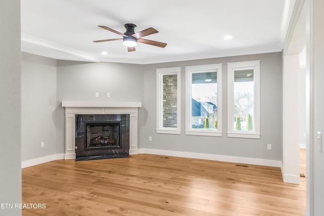 unfurnished living room with ornamental molding, a high end fireplace, ceiling fan, and light wood-type flooring