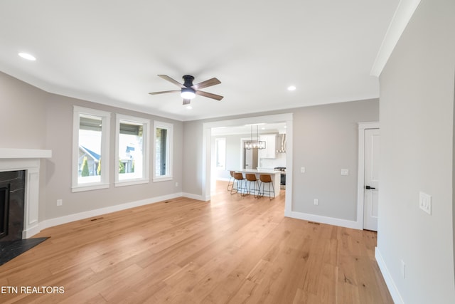 unfurnished living room with ceiling fan, ornamental molding, a fireplace, and light hardwood / wood-style flooring