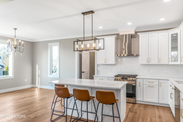 kitchen with a kitchen island, white cabinetry, hanging light fixtures, stainless steel appliances, and wall chimney exhaust hood