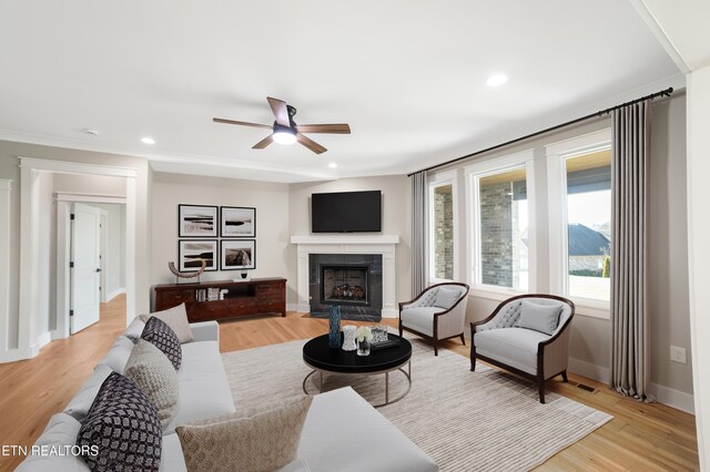 living room featuring a ceiling fan, baseboards, a tiled fireplace, and light wood-type flooring