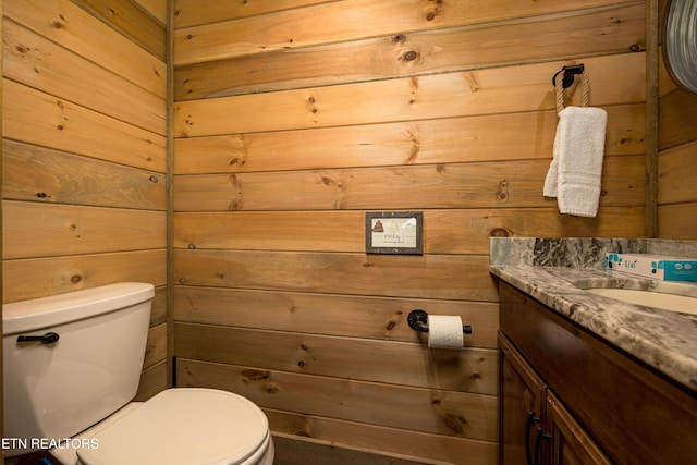 bathroom featuring vanity, toilet, and wood walls