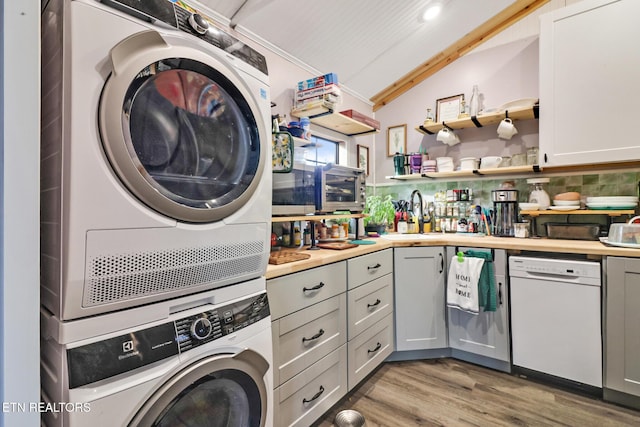 laundry area with stacked washer and dryer, hardwood / wood-style flooring, and sink