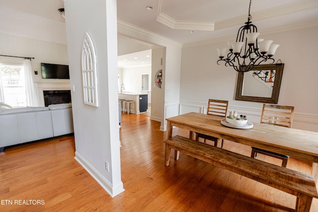 dining room with a chandelier, ornamental molding, a raised ceiling, and light hardwood / wood-style floors