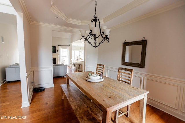 dining space with ornamental molding, wood-type flooring, a tray ceiling, and a notable chandelier