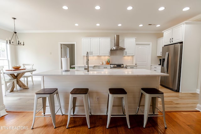 kitchen with wall chimney range hood, white cabinets, a spacious island, and appliances with stainless steel finishes