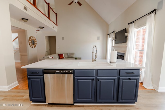 kitchen featuring blue cabinets, an island with sink, sink, stainless steel dishwasher, and light hardwood / wood-style floors