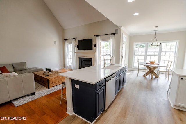 kitchen featuring a breakfast bar, sink, hanging light fixtures, stainless steel dishwasher, and an island with sink