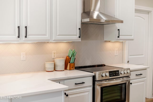 kitchen with tasteful backsplash, white cabinetry, electric range, and wall chimney exhaust hood