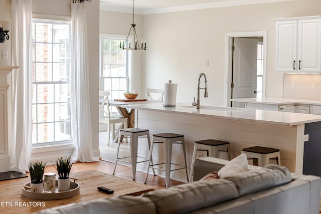 kitchen featuring sink, crown molding, hanging light fixtures, white cabinets, and a kitchen bar