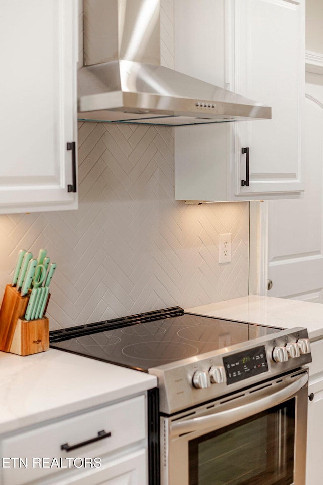 kitchen featuring white cabinets, stainless steel electric range, decorative backsplash, and wall chimney exhaust hood