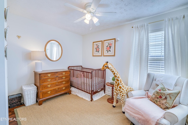 bedroom with ceiling fan, a nursery area, and a textured ceiling