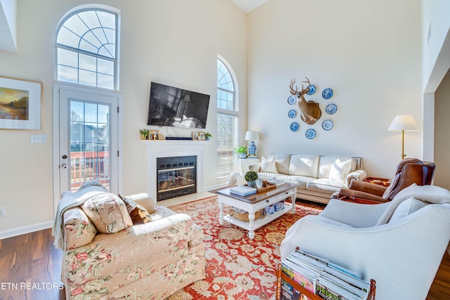 living room with dark wood-type flooring, a towering ceiling, and a wealth of natural light