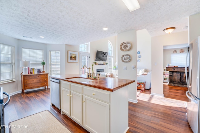 kitchen with sink, dark wood-type flooring, white cabinetry, stainless steel appliances, and a center island with sink