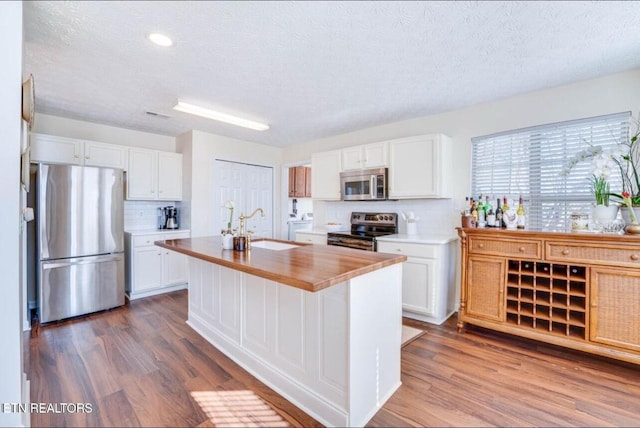 kitchen featuring stainless steel appliances, white cabinetry, dark hardwood / wood-style floors, and an island with sink