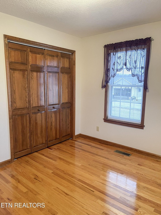 unfurnished bedroom featuring a closet, light hardwood / wood-style flooring, and a textured ceiling