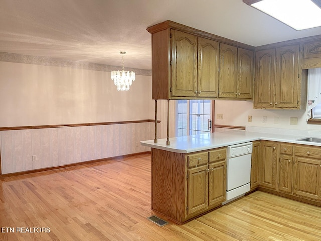 kitchen featuring an inviting chandelier, decorative light fixtures, light wood-type flooring, white dishwasher, and kitchen peninsula