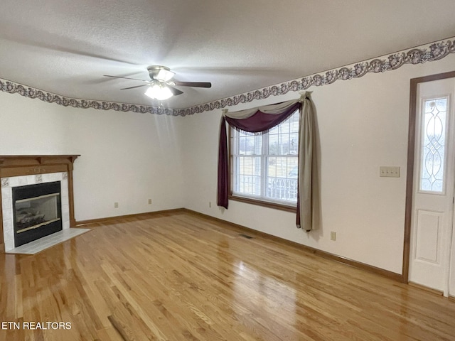 unfurnished living room featuring a tile fireplace, hardwood / wood-style floors, ceiling fan, and a textured ceiling