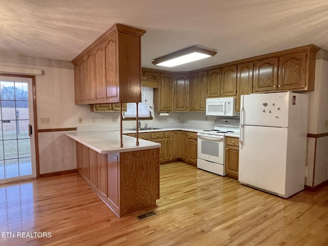 kitchen with sink, a kitchen breakfast bar, kitchen peninsula, white appliances, and light hardwood / wood-style floors