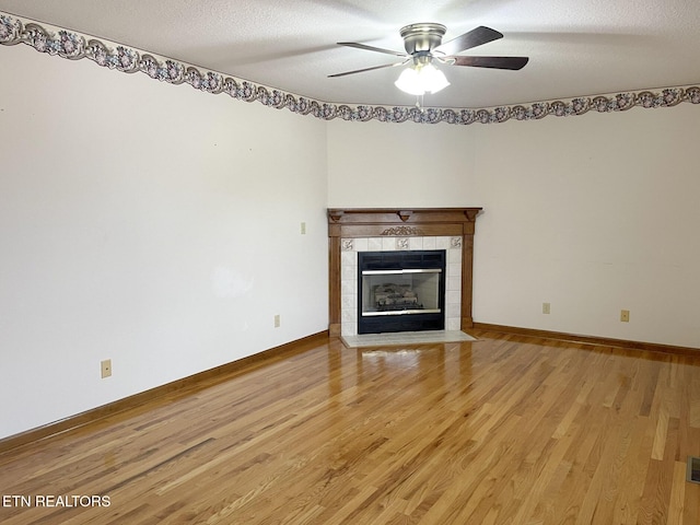 unfurnished living room with ceiling fan, light hardwood / wood-style flooring, a tile fireplace, and a textured ceiling