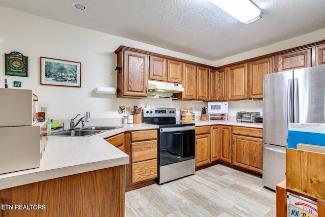 kitchen with appliances with stainless steel finishes, sink, a textured ceiling, and light wood-type flooring