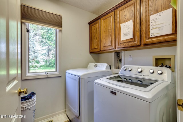 clothes washing area with cabinets, washing machine and clothes dryer, and a textured ceiling