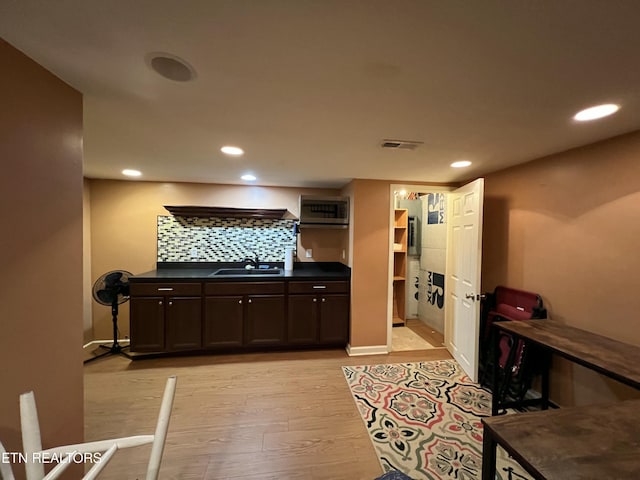 kitchen featuring sink, backsplash, dark brown cabinetry, and light wood-type flooring