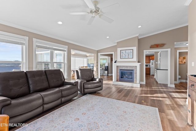 living room featuring crown molding, vaulted ceiling, ceiling fan, a tiled fireplace, and hardwood / wood-style floors