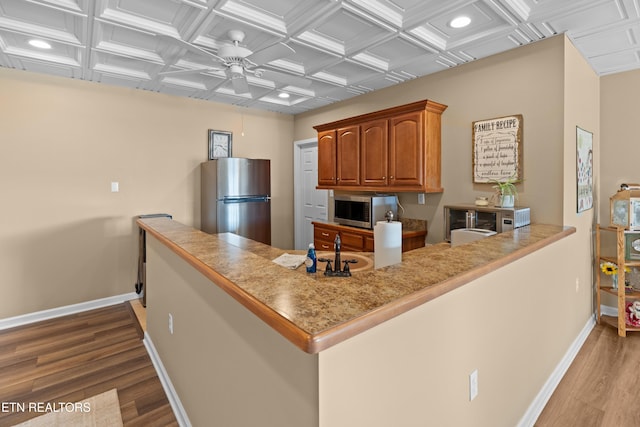 kitchen with stainless steel appliances, ceiling fan, light hardwood / wood-style floors, and kitchen peninsula