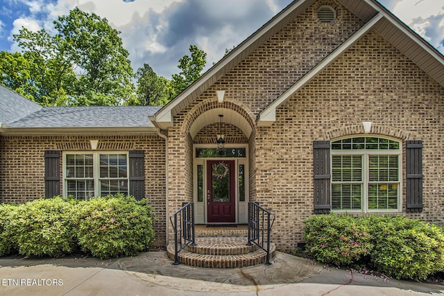 view of exterior entry featuring brick siding and roof with shingles