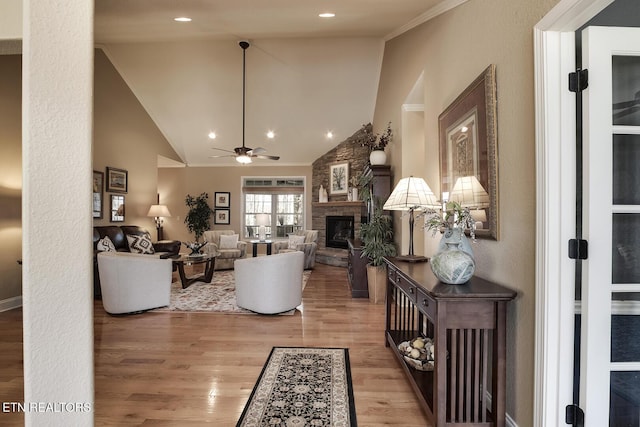 living area with light wood-type flooring, a stone fireplace, ceiling fan, crown molding, and vaulted ceiling