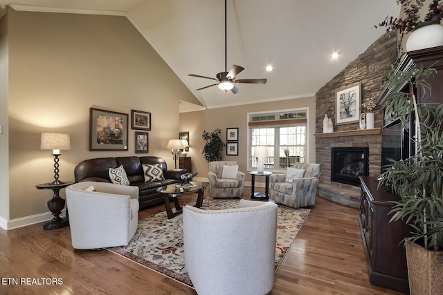living area featuring baseboards, ceiling fan, wood finished floors, a stone fireplace, and crown molding