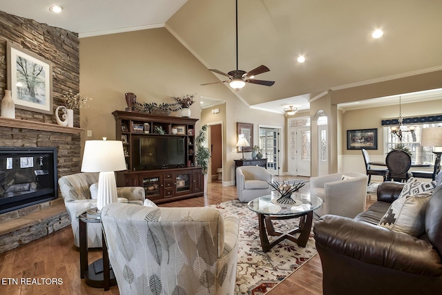 living room with ornamental molding, a ceiling fan, a stone fireplace, wood finished floors, and a chandelier