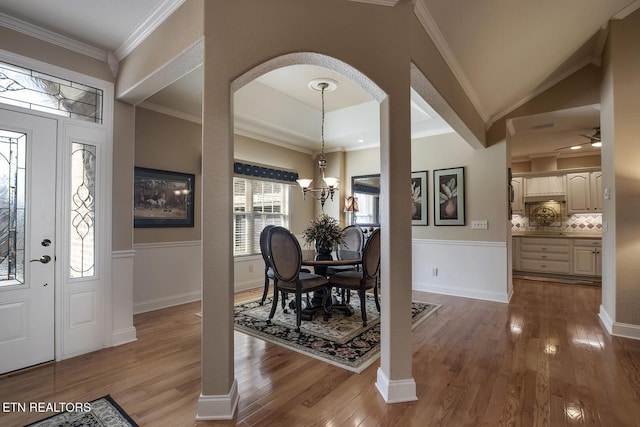 foyer entrance featuring wood finished floors, arched walkways, ornamental molding, and a chandelier