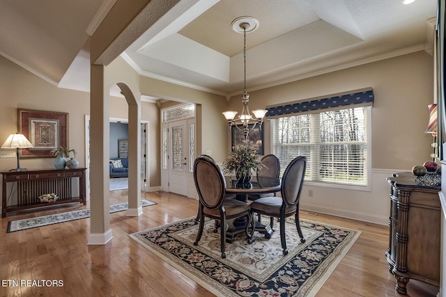 dining area featuring light wood-style flooring, a raised ceiling, baseboards, ornamental molding, and a chandelier