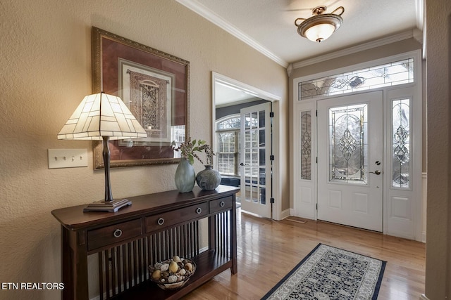 foyer with crown molding, wood finished floors, a textured wall, and baseboards