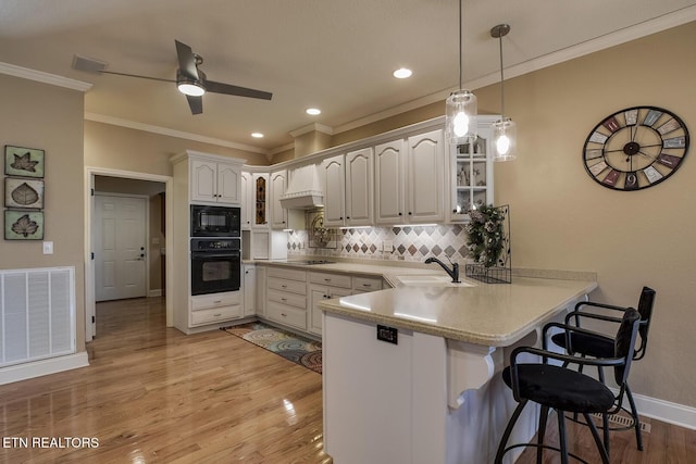 kitchen featuring black appliances, a peninsula, a sink, a kitchen bar, and crown molding