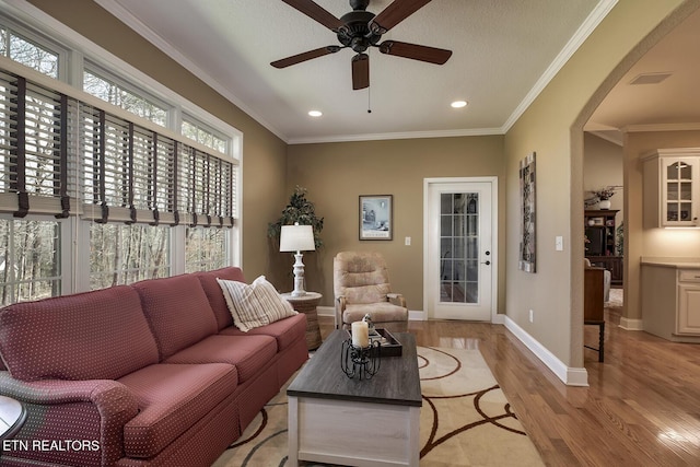 living area with light wood-type flooring, ceiling fan, arched walkways, recessed lighting, and baseboards