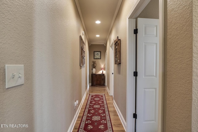 corridor with light wood-type flooring, crown molding, a textured wall, recessed lighting, and baseboards