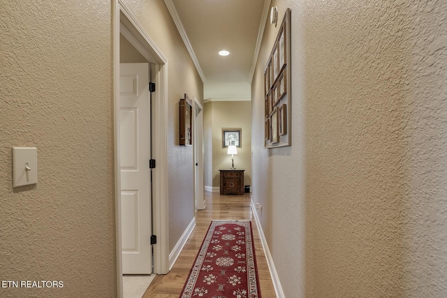 corridor featuring a textured wall, light wood-style floors, ornamental molding, baseboards, and recessed lighting