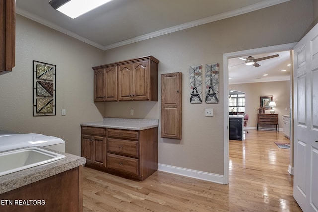 laundry area featuring ornamental molding, cabinet space, light wood-style floors, a ceiling fan, and baseboards