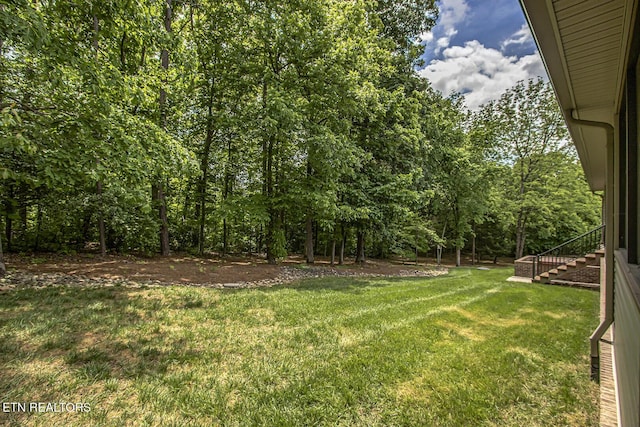 view of grassy yard featuring stairway and a wooded view