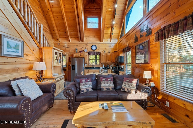 living room with sink, light hardwood / wood-style flooring, wooden walls, high vaulted ceiling, and beamed ceiling