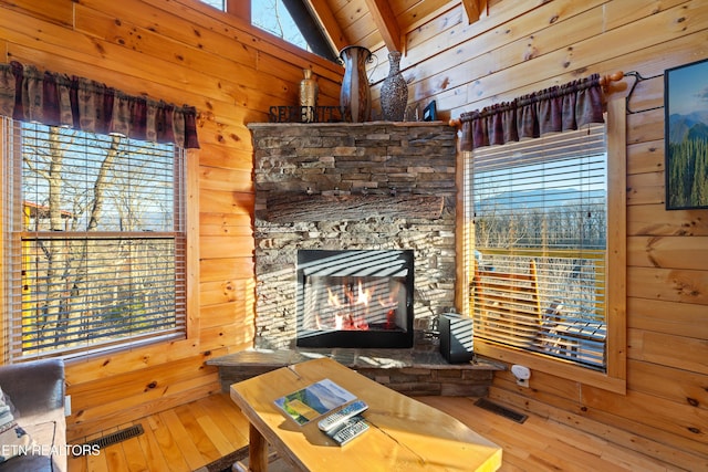 unfurnished living room featuring hardwood / wood-style flooring, a stone fireplace, wooden ceiling, and wood walls