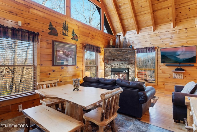 dining area featuring beam ceiling, a stone fireplace, wooden ceiling, and wood walls