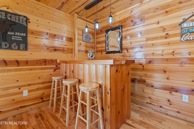 bar featuring wood ceiling, decorative light fixtures, light hardwood / wood-style floors, and wood walls