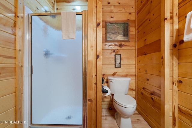 bathroom with toilet, hardwood / wood-style floors, an enclosed shower, and wood walls