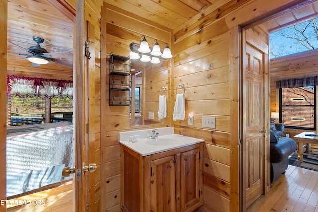 bathroom featuring wooden walls, wood-type flooring, vanity, ceiling fan, and wood ceiling