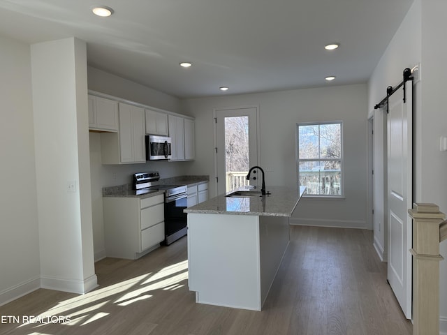 kitchen with white cabinetry, sink, stainless steel appliances, a barn door, and a center island with sink