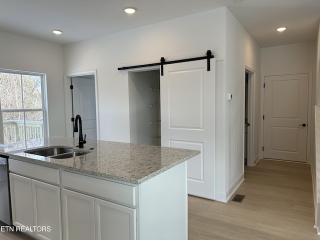 kitchen with sink, white cabinetry, a barn door, light stone countertops, and a kitchen island with sink